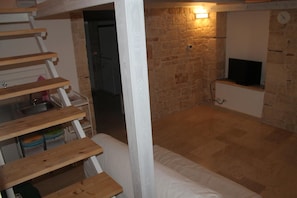 A room with a stone wall, a television mounted on the wall, and a wooden staircase. - B&B Piazza Garibaldi (Santeramo in Colle)