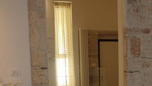 A hotel room with a stone wall, a bed, a small table, and a bathroom with a shower and toilet. - B&B Piazza Garibaldi (Santeramo in Colle)