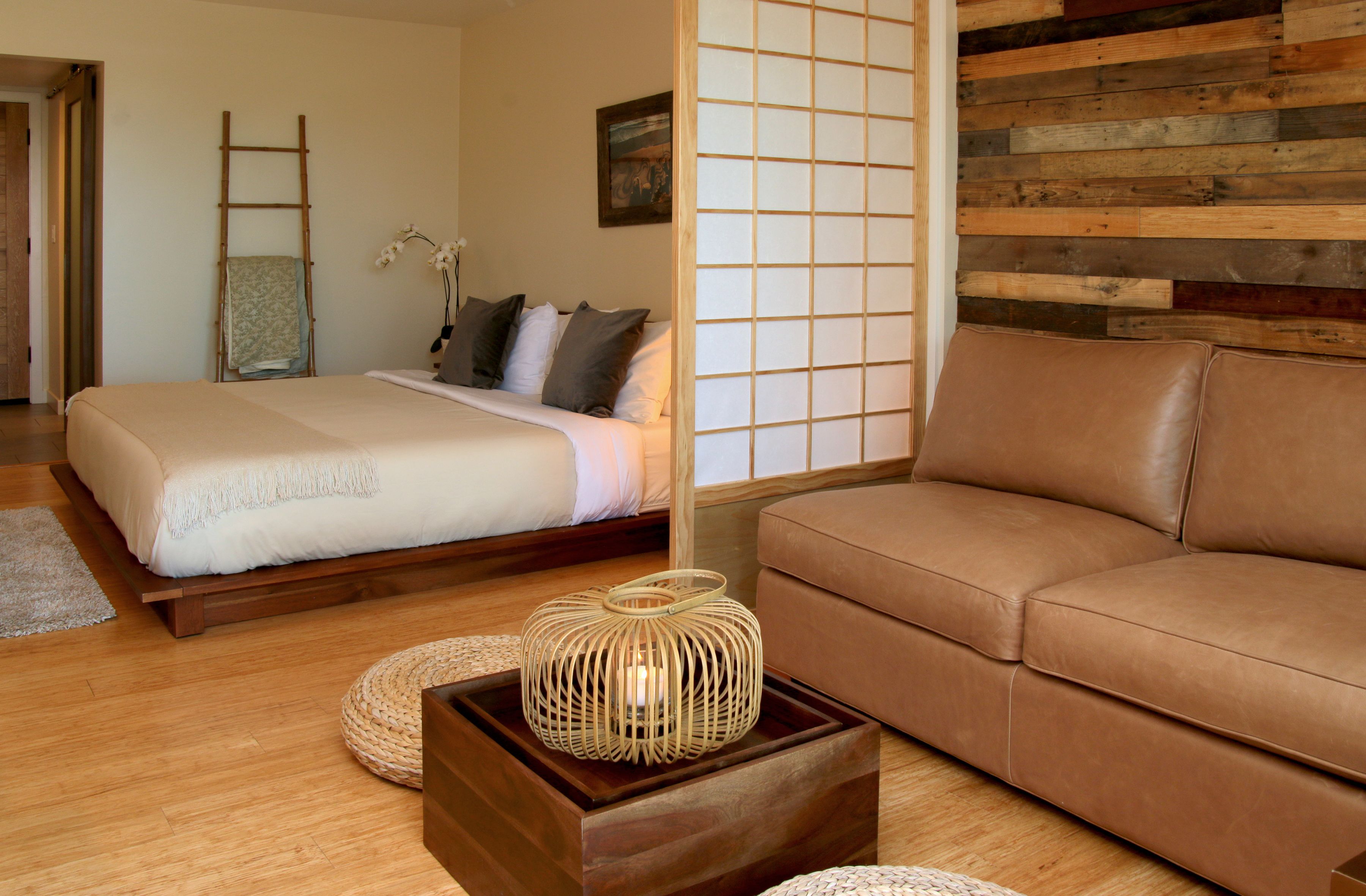 Un dormitorio con cama, una escalera de madera, un separador de madera, un sofá marrón y una lámpara tejida sobre una mesa de madera.