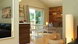 A modern living room with a wooden floor, a black leather sofa, a white table with chairs, and a wicker side table. - Inn at Moonlight Beach (Encinitas)