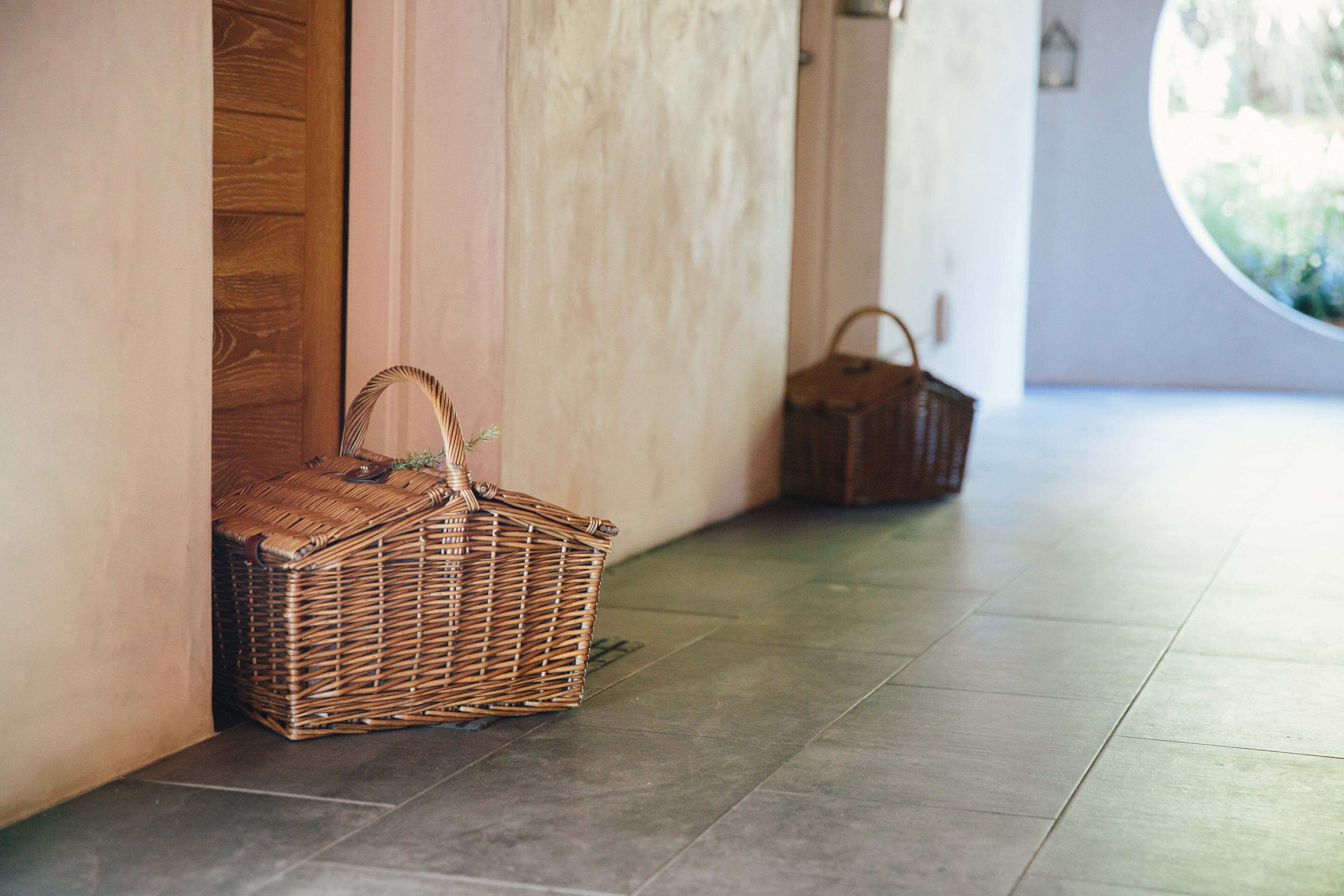 Un panier en osier est posé sur un sol carrelé, à côté d’une porte en bois.
