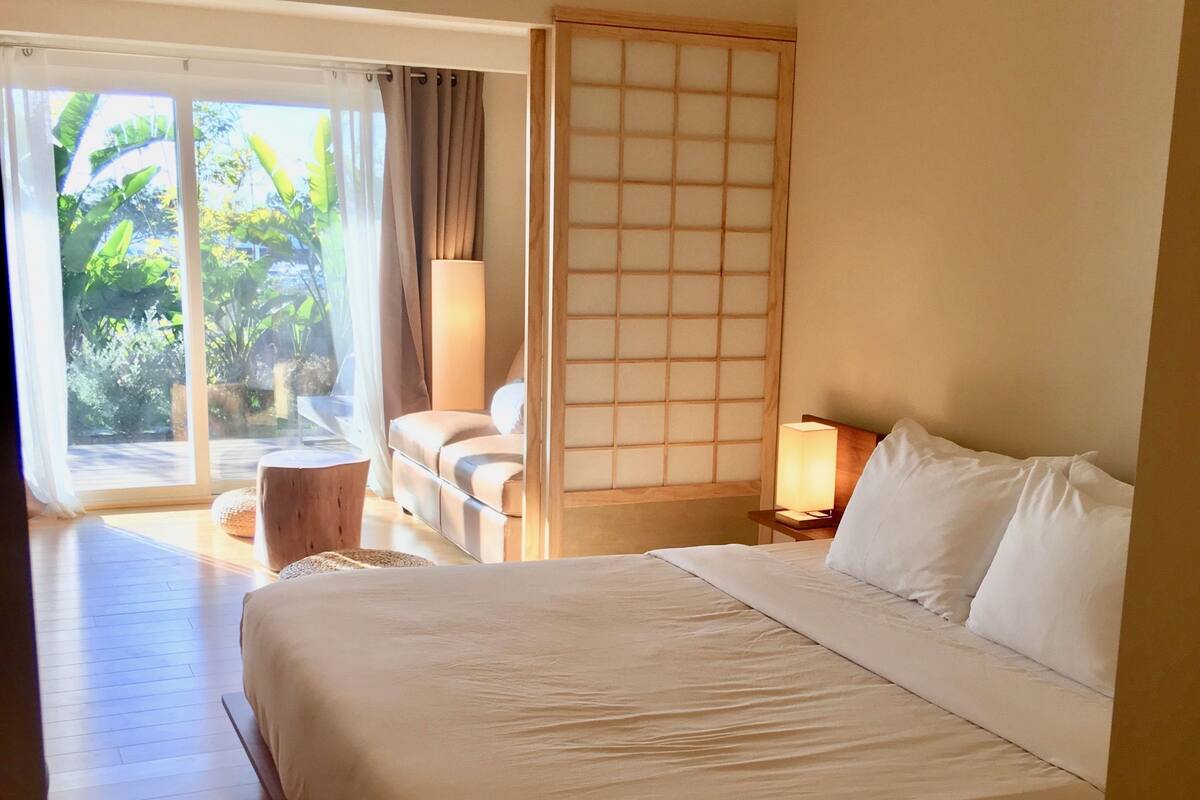A hotel room with a large bed, a seating area with a sofa and a small table, a sliding glass door leading to a balcony, and a traditional Japanese-style shoji screen.