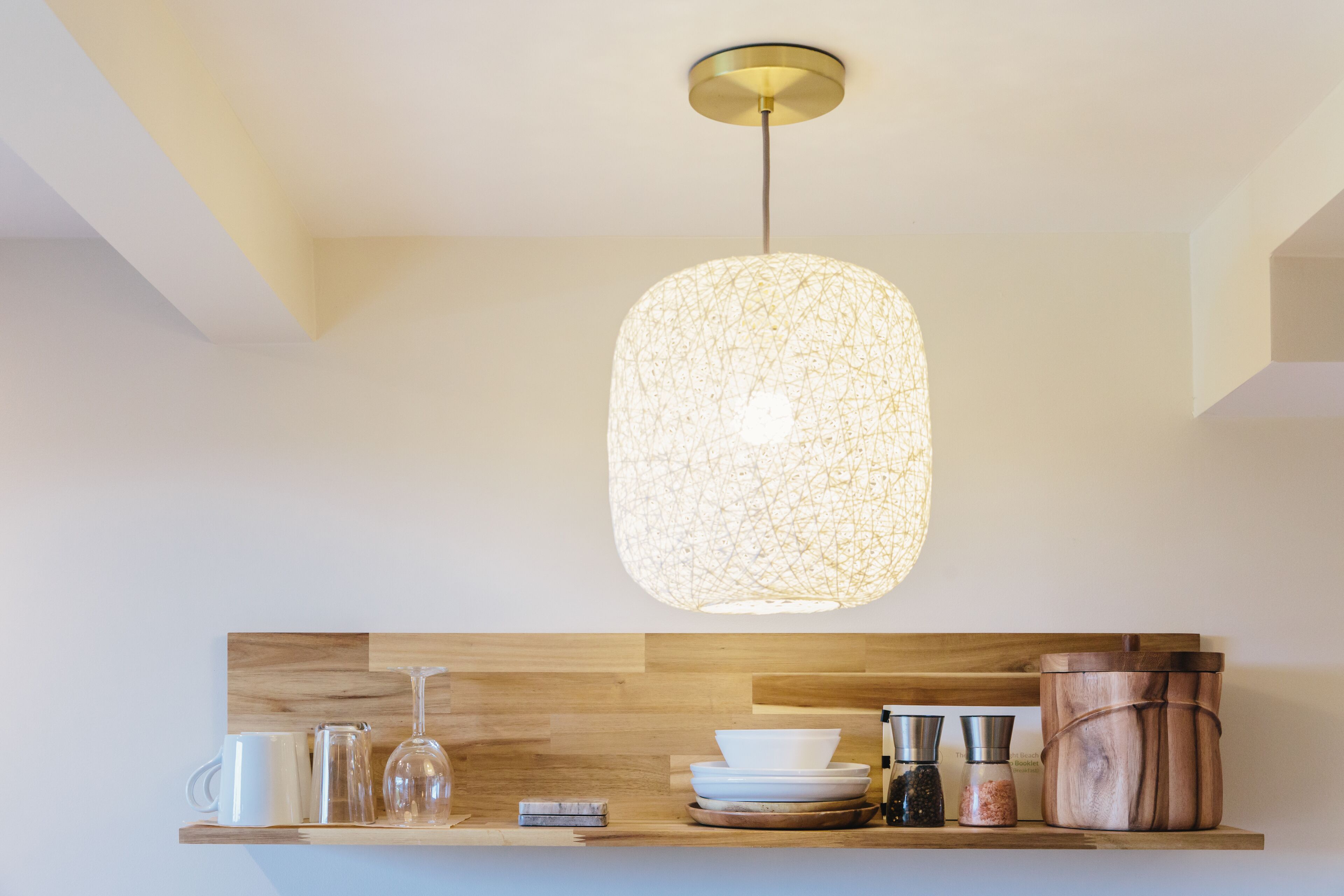 Una cocina moderna con una lámpara colgante, estantes de madera y diferentes utensilios de cocina.