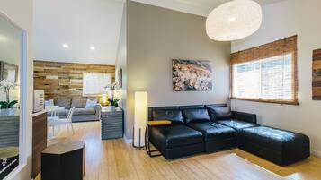 Een moderne woonkamer met een hoekbank, een eethoek met een witte tafel en stoelen, en een groot raam met bamboeblamen.