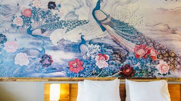 Un mural tradicional con pavos reales y flores en una pared, sobre una cama con almohadas blancas.