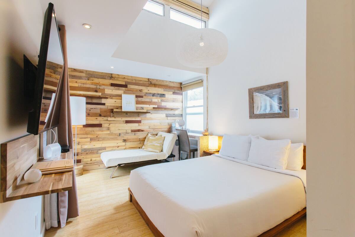 A modern hotel room with a wooden wall, a bed, a desk, and a TV.