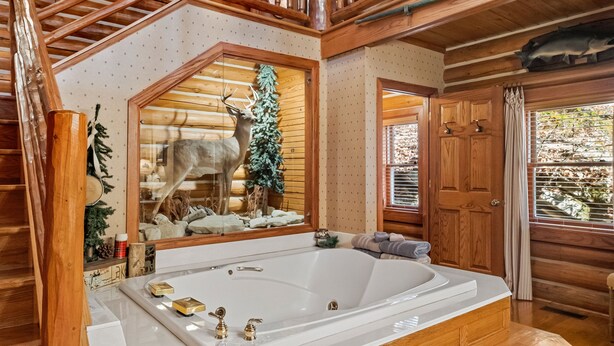 A log cabin interior with a large wooden staircase, a wooden balcony, a fireplace, and a large bathtub. - Cinnamon Valley Resort (Eureka Springs)
