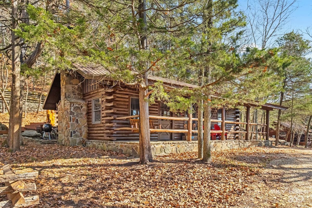 A rustic log cabin with a stone foundation, wooden deck, and a covered outdoor seating area.