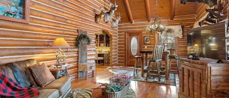 L’intérieur d’une cabane en rondins présente un plafond en bois, un coin repas, un salon avec un canapé et un téléviseur, ainsi qu’une tête d’élan fixée au mur.