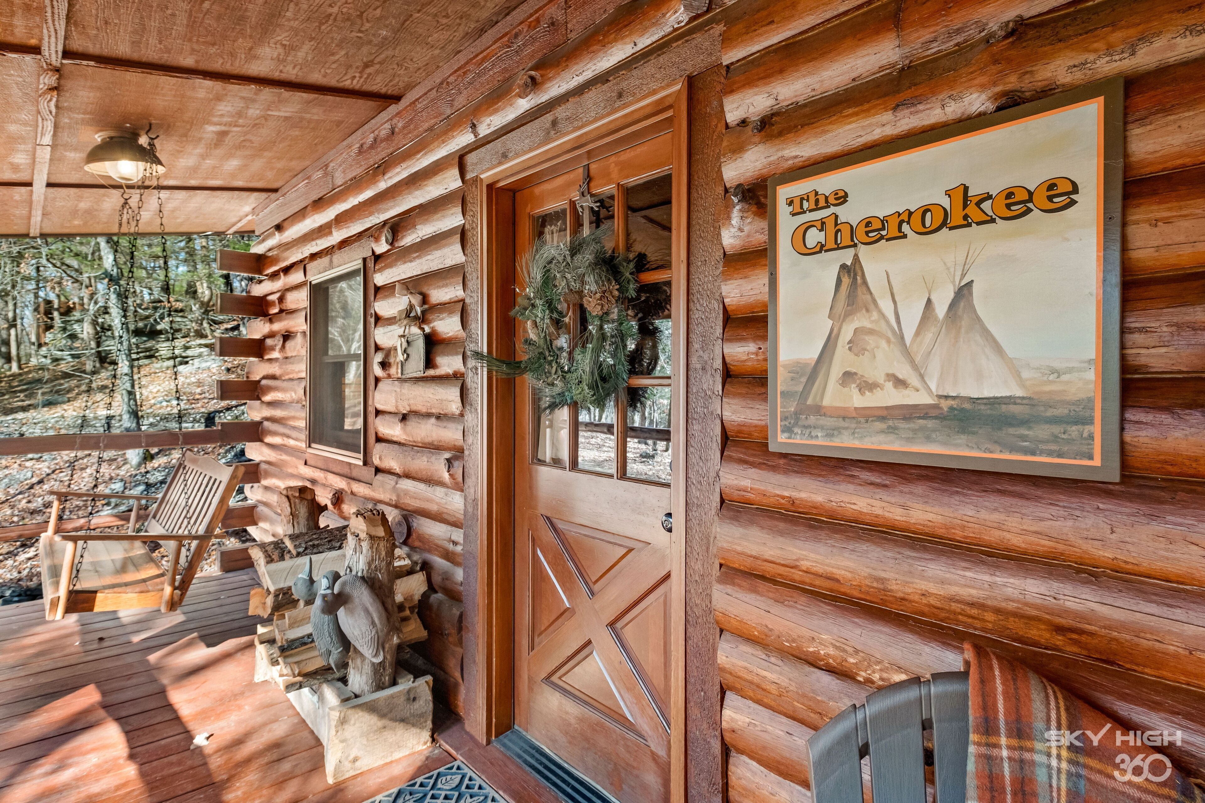 Une cabane en bois avec un porche, une porte ornée d’une croix et une affiche représentant des tipis, sur laquelle on peut lire : « Les Cherokees ».