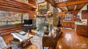 A cozy log cabin interior with a stone fireplace, wooden furnishings, and a stone wall with a painting. - Cinnamon Valley Resort (Eureka Springs)