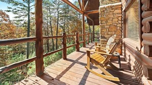 A wooden deck with a stone wall and a wooden railing. - Cinnamon Valley Resort (Eureka Springs)