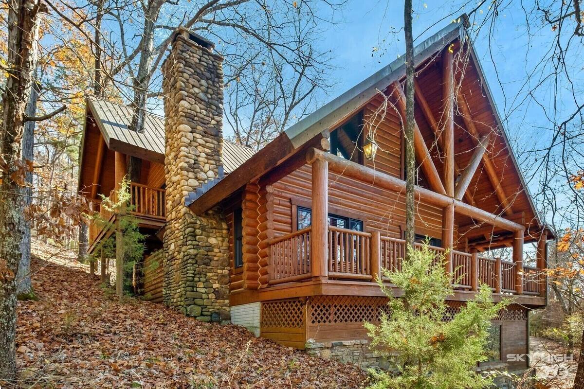 A log cabin with a stone chimney, wooden deck, and a stone foundation.