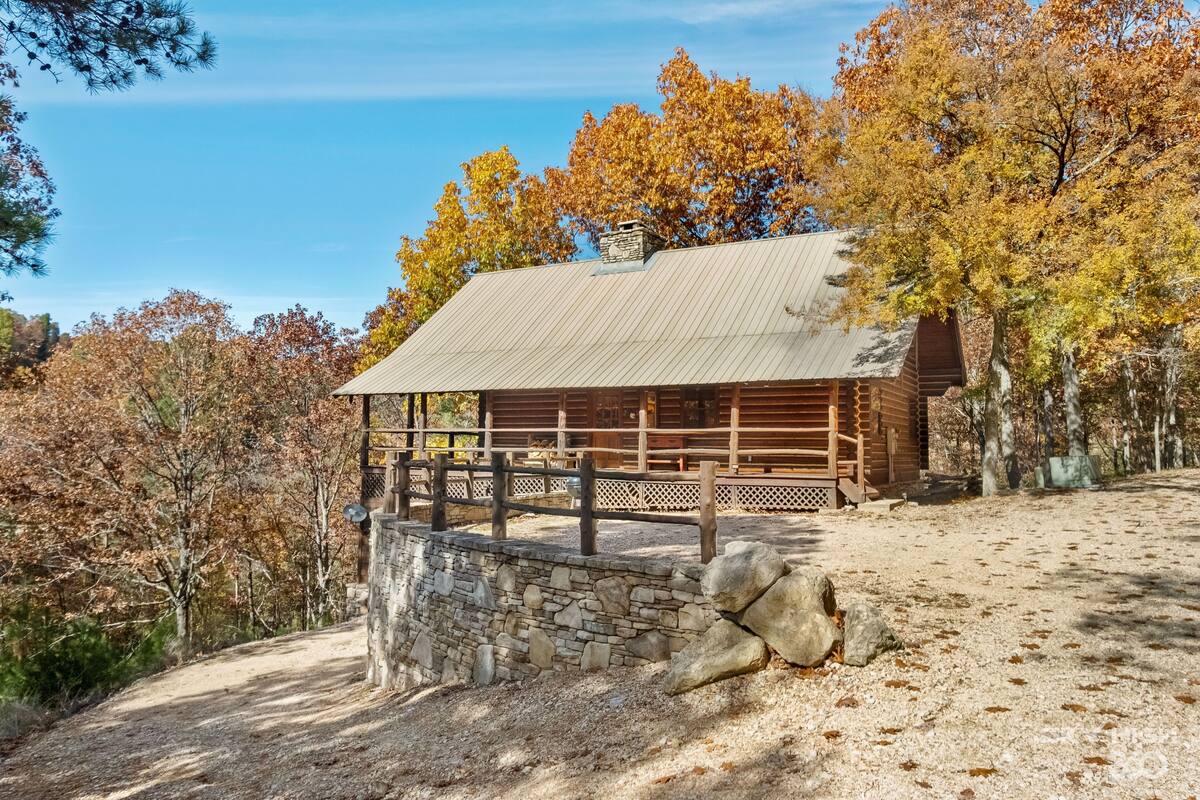 A rustic cabin with a stone wall and wooden fence, surrounded by autumn foliage.