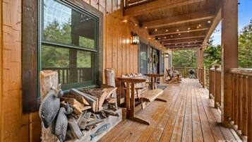 A wooden deck with outdoor seating, a large window, and a pile of firewood.