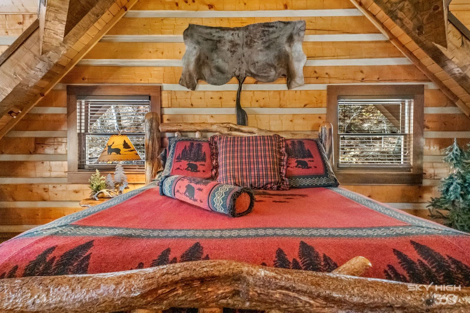 A cozy log cabin bedroom with a bed, pillows, and a mounted animal hide.