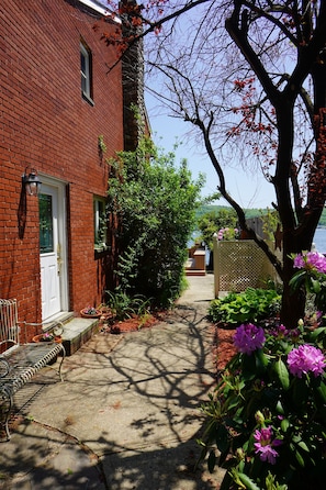 Stroll through the beautifully maintained garden, surrounded by lush plants and flowers, to a scenic view beyond the wooden fence.