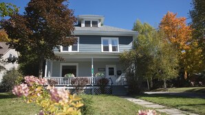A two-story house with a front porch, a small staircase leading to the entrance, and a clear sky. - Lake Placid Home in the Heart of Adirondack Village
 (Lake Placid)