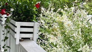 A white wooden balcony with a planter filled with green foliage and red flowers. - Lake Placid Home in the Heart of Adirondack Village
 (Lake Placid)