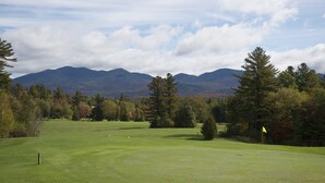 A golf course with a flagstick, trees, and mountains in the background. - Lake Placid Home in the Heart of Adirondack Village
 (Lake Placid)