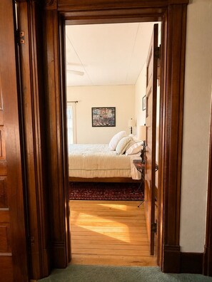 Un dormitorio con cama, mesita de noche, lámpara y un cuadro en la pared.