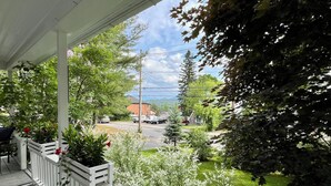 A porch with a railing, potted plants, and a view of a street with cars and houses. - Lake Placid Home in the Heart of Adirondack Village
 (Lake Placid)