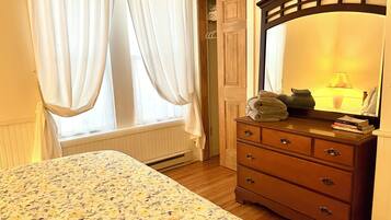 A bedroom with a bed, a dresser, a mirror, and a window with curtains.