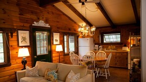 A cozy cabin interior with a wooden dining area, a sofa with floral cushions, and a kitchen with wooden cabinets. -  Charming, Eco-Friendly Cabin Retreat, Heart of Deep Creek (Oakland)
