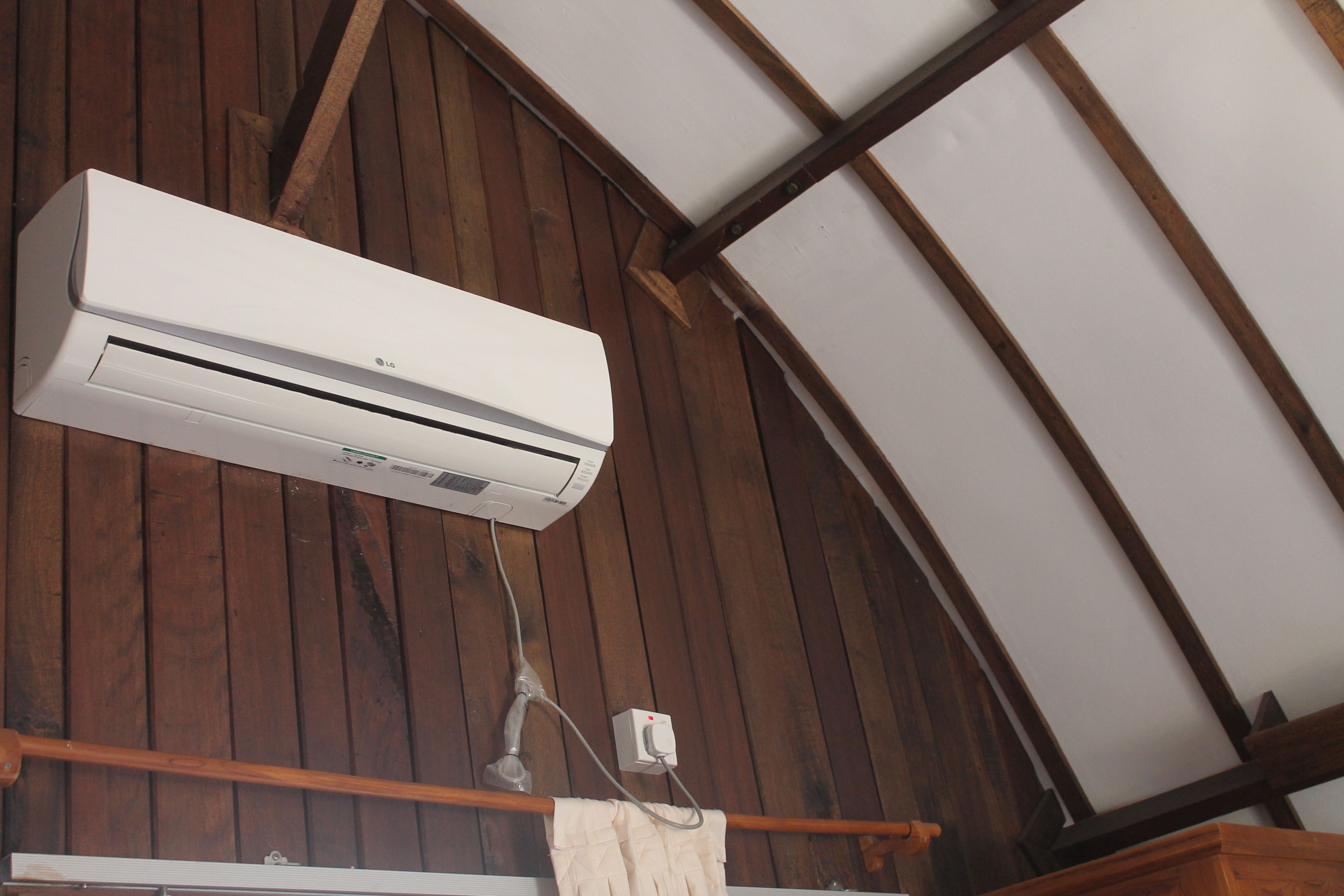 Un appareil de climatisation fixé au plafond en bois, dont les poutres apparentes sont visibles.
