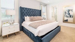 Quarto com cabeceira estofada, mesa de cabeceira branca, cama grande com manta fofa e espelho na parede.