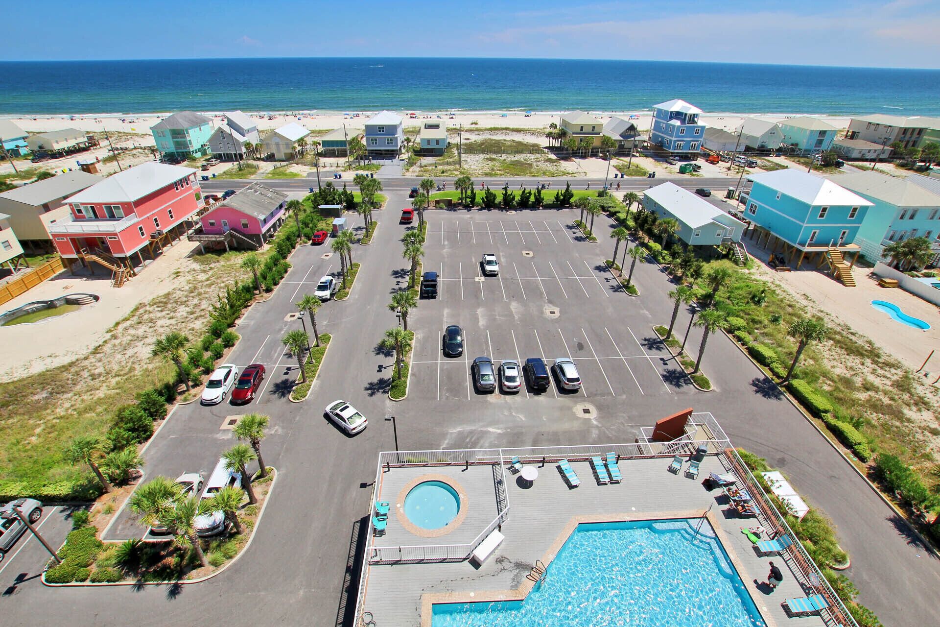 An aerial view of a coastal hotel with a parking lot, a swimming pool, and beach access.