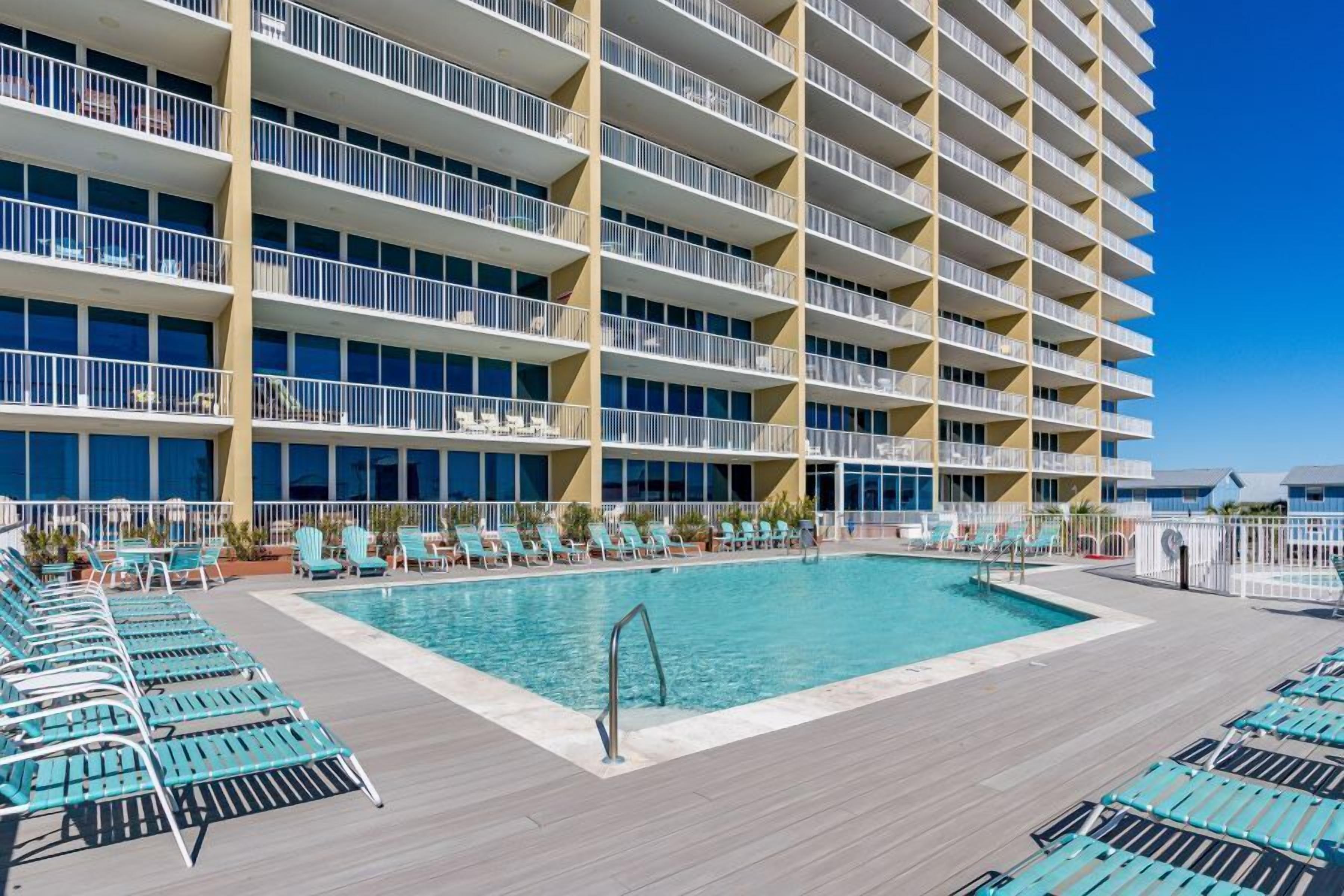A hotel with a large pool area, multiple balconies, and sun loungers.