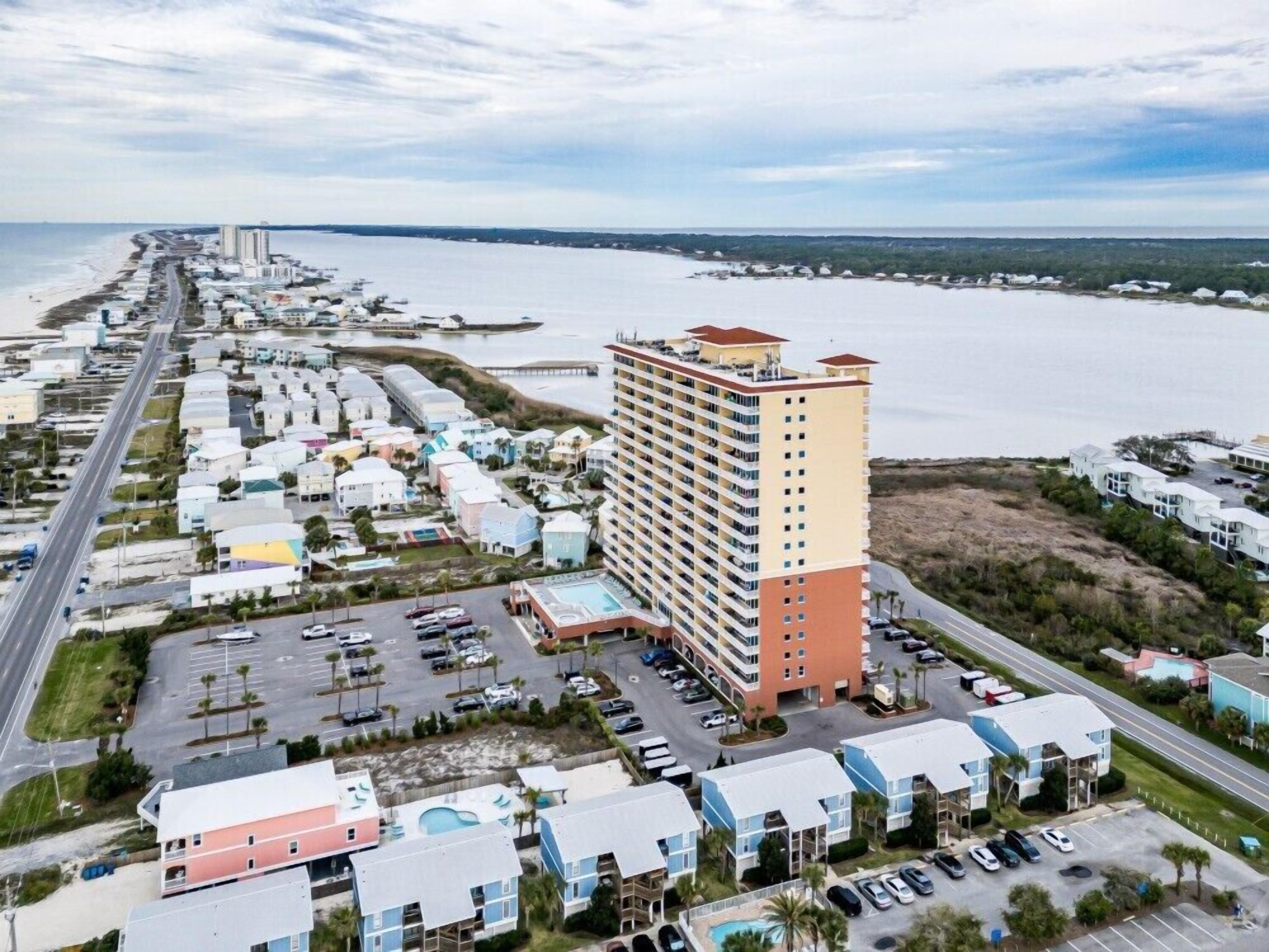 A coastal hotel with a central building, multiple parking lots, and a view of the ocean.