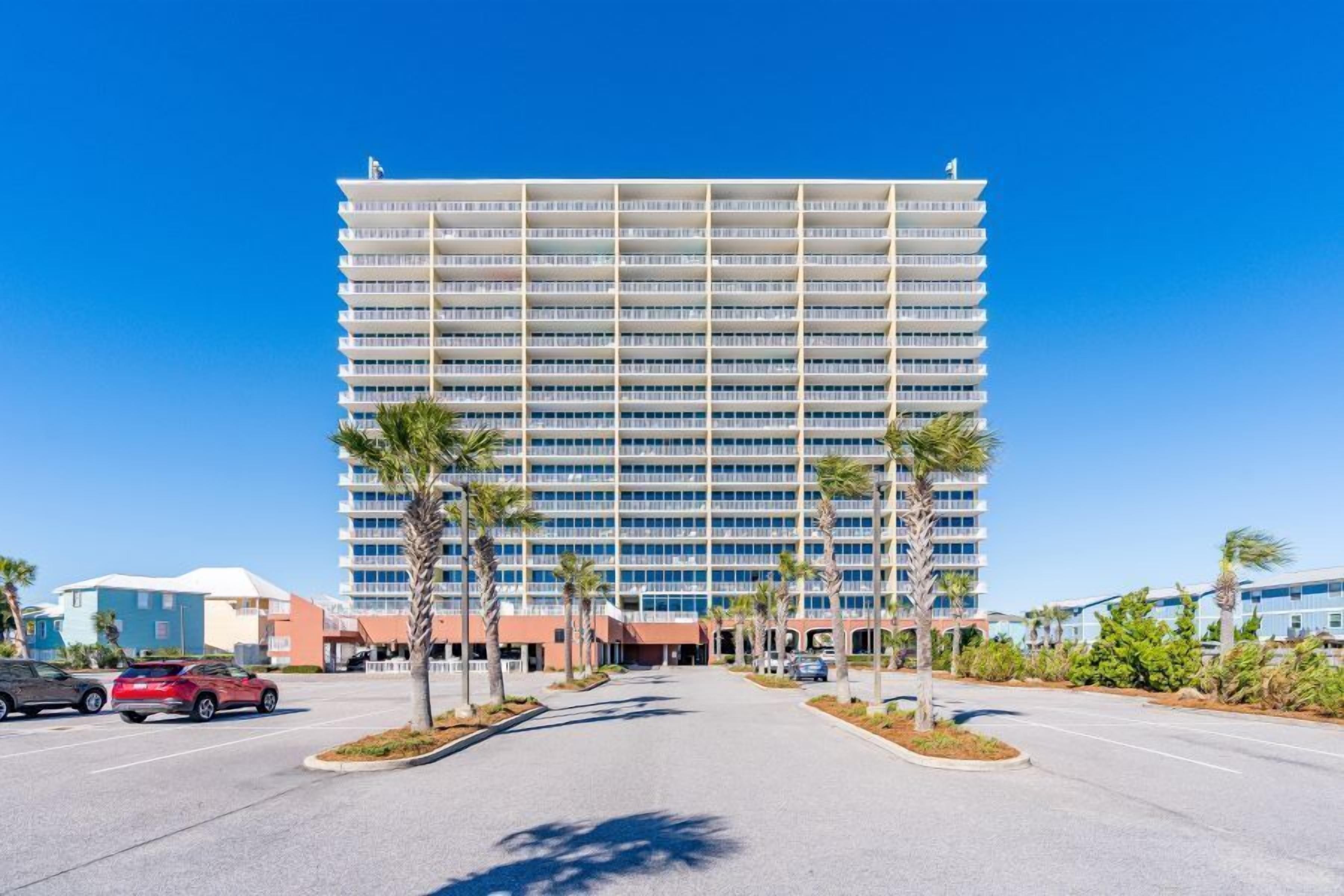 A multi-story hotel with a central courtyard, palm trees, and a parking lot.
