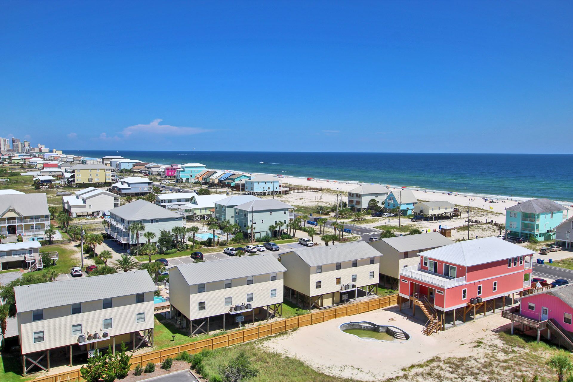 Un quartier résidentiel situé sur la côte, avec des propriétés donnant sur la plage, notamment des maisons construites sur des fondations surélevées et une route longeant la plage.