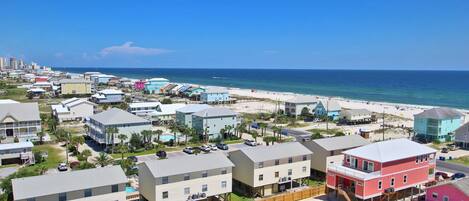 Un quartier résidentiel situé sur la côte, avec des propriétés donnant sur la plage, notamment des maisons construites sur des fondations surélevées et une route longeant la plage.