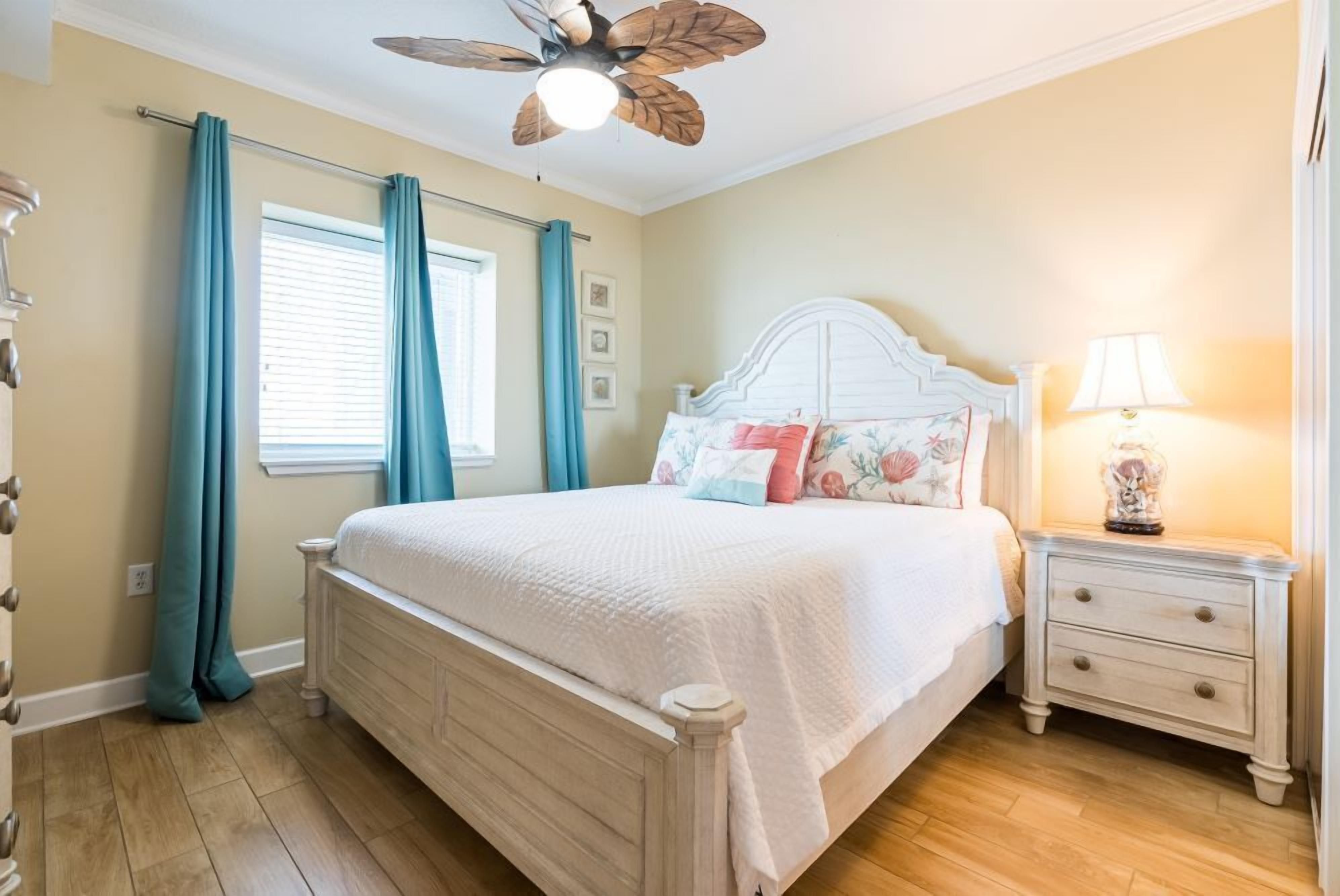 Een slaapkamer met een bed, nachtkastje, plafondventilator en een raam met gordijnen.