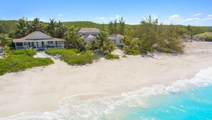Une propriété située en bord de mer, comprenant plusieurs maisons, une plage de sable et un océan d’un bleu limpide.