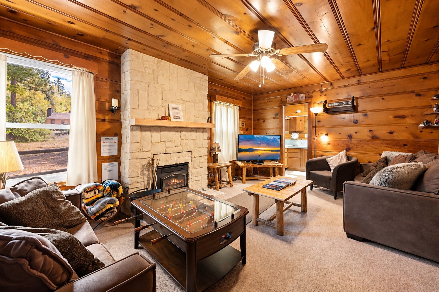 A cozy cabin interior with a stone fireplace, a foosball table, a television, and a comfortable seating area.