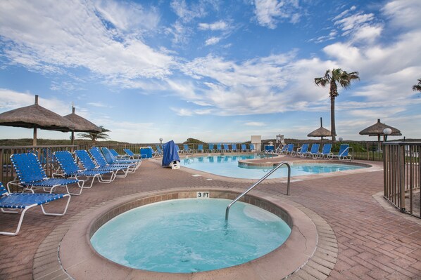 A pool area with lounge chairs and umbrellas, a hot tub, and a palm tree.