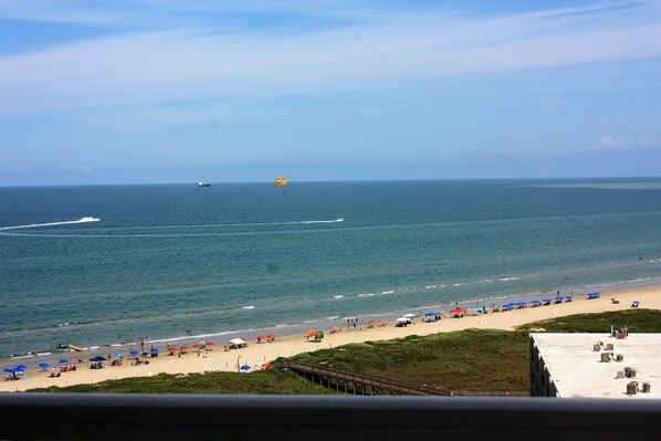 A beach with umbrellas and people, a pier, and a ship in the distance.