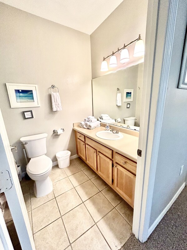 Une salle de bain avec des toilettes, un lavabo et un meuble de rangement. Des serviettes sont suspendues à des crochets et un tableau encadré est accroché au mur.