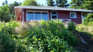 A single-story house with a red exterior, a front porch, and a garage. - Secluded Oceanfrot cottage:Unbelievable oceanfront views-Screened in Gazebo (Wilsons Beach, Campobello Island)