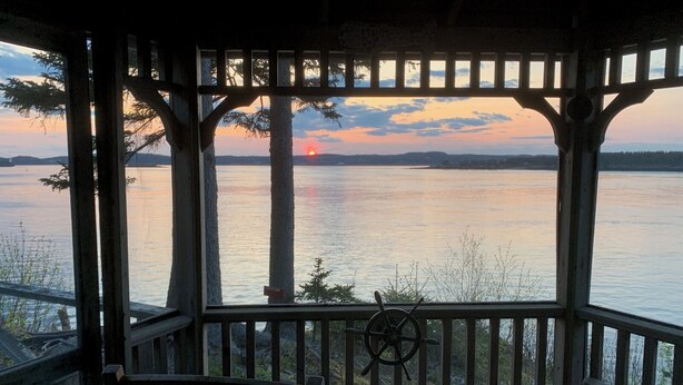 A wooden gazebo with a view of a sunset over a calm lake. - Secluded Oceanfrot cottage:Unbelievable oceanfront views-Screened in Gazebo (Wilsons Beach, Campobello Island)
