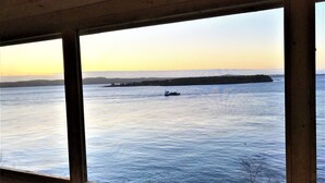 A view from a window overlooking a calm body of water with a distant shoreline and a small boat. - Secluded Oceanfrot cottage:Unbelievable oceanfront views-Screened in Gazebo (Wilsons Beach, Campobello Island)