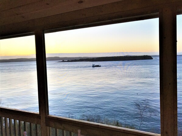 A view from a window overlooking a calm body of water with a distant shoreline and a small boat. - Secluded Oceanfrot cottage:Unbelievable oceanfront views-Screened in Gazebo (Wilsons Beach, Campobello Island)