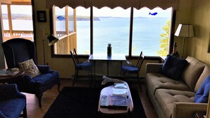 A living room with a view of the sea, a table with books, and two sofas. - Secluded Oceanfrot cottage:Unbelievable oceanfront views-Screened in Gazebo (Wilsons Beach, Campobello Island)