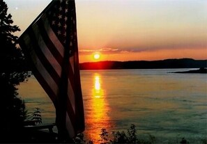 A sunset over a calm body of water with an American flag in the foreground. - Secluded Oceanfrot cottage:Unbelievable oceanfront views-Screened in Gazebo (Wilsons Beach, Campobello Island)