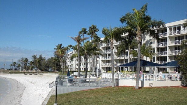 Ein Strandhotel mit mehreren Balkonen, Palmen und einem Sandstrand.