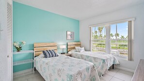 A hotel room with two beds, a window with a view of palm trees, and a small table with a vase of flowers.